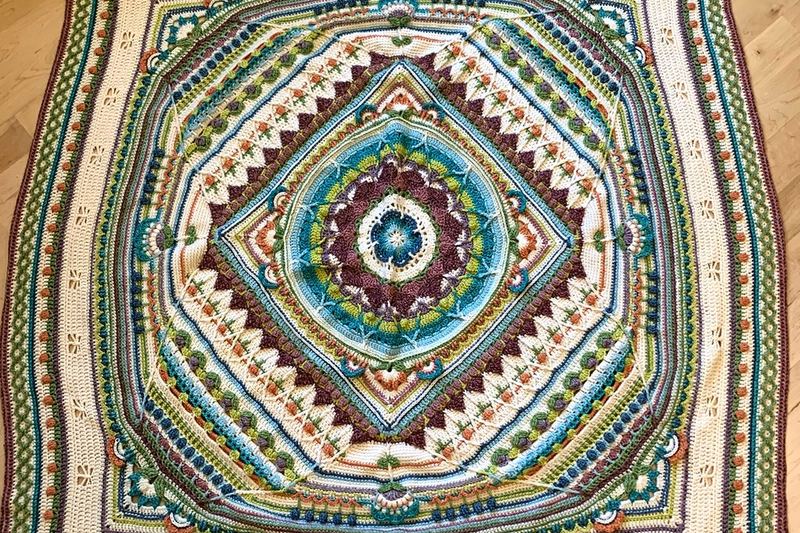 Manta de crochet cuadrada con vueltas concéntricas de colores, extendida completamente plana sobre el suelo